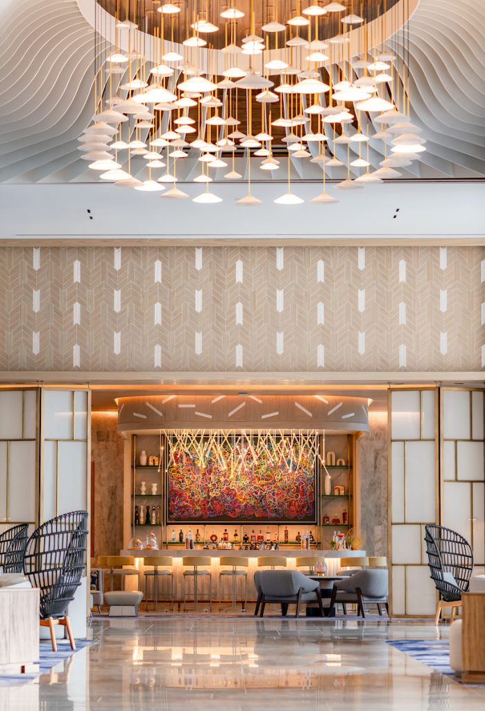 A clean, elegant lobby beautifully decorated with a grand chandelier hanging center.