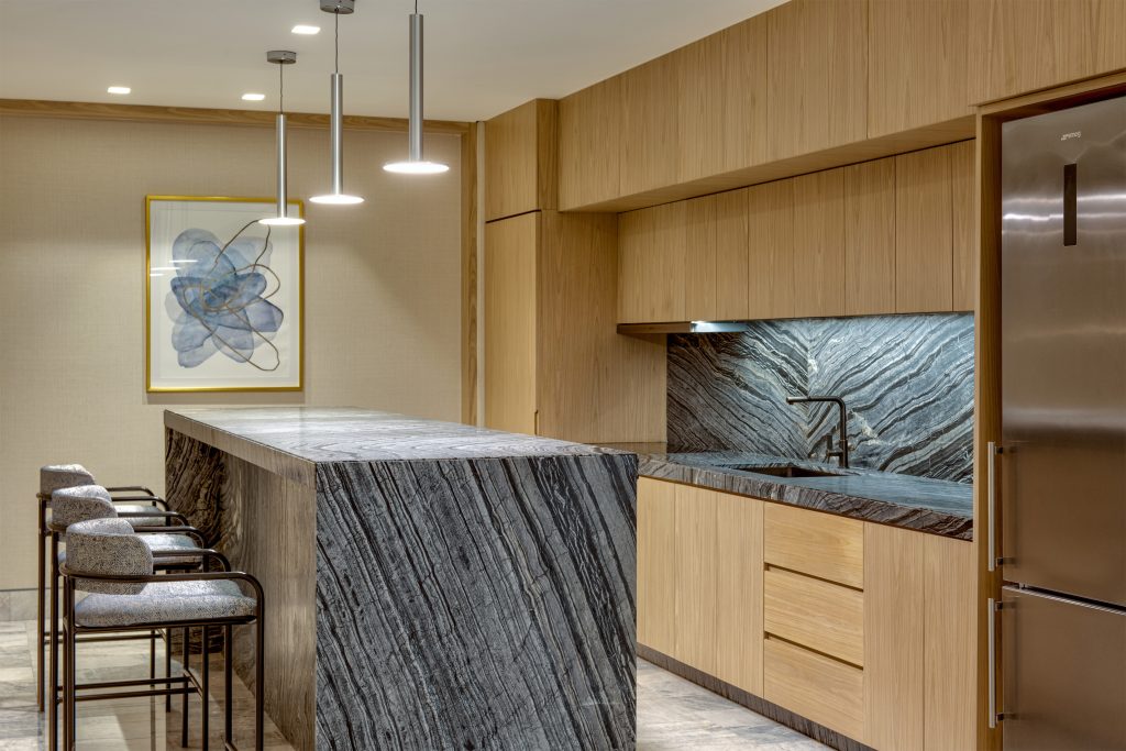 Three cozy chairs sit by the kitchen countertop, portrait mounted on the wall.