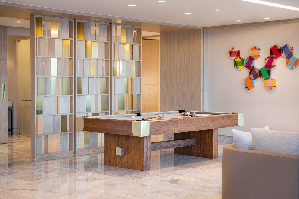 A billiards table stands near glass partition, with crafted paper design on wall.