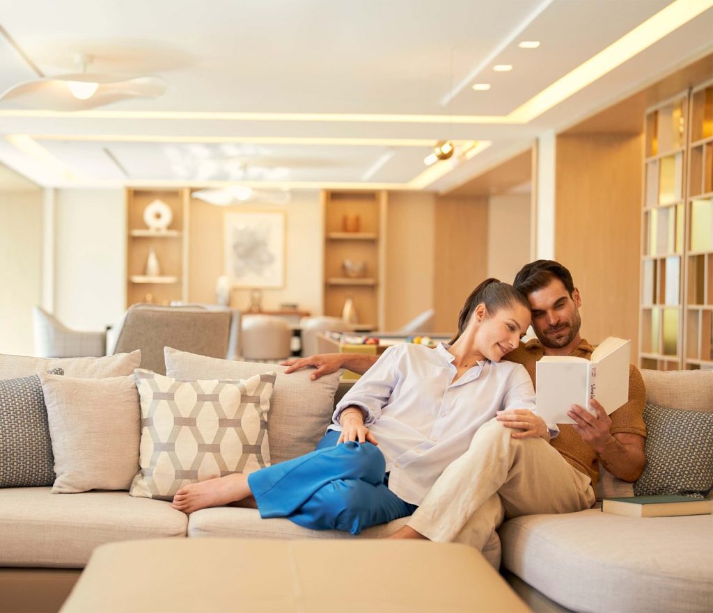 A couple lying on cozy sofa, reading a book together peacefully.