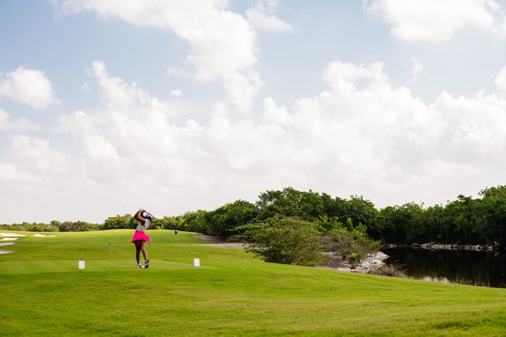 A lady playing golf gracefully on vibrant, green, well-maintained grassy ground.