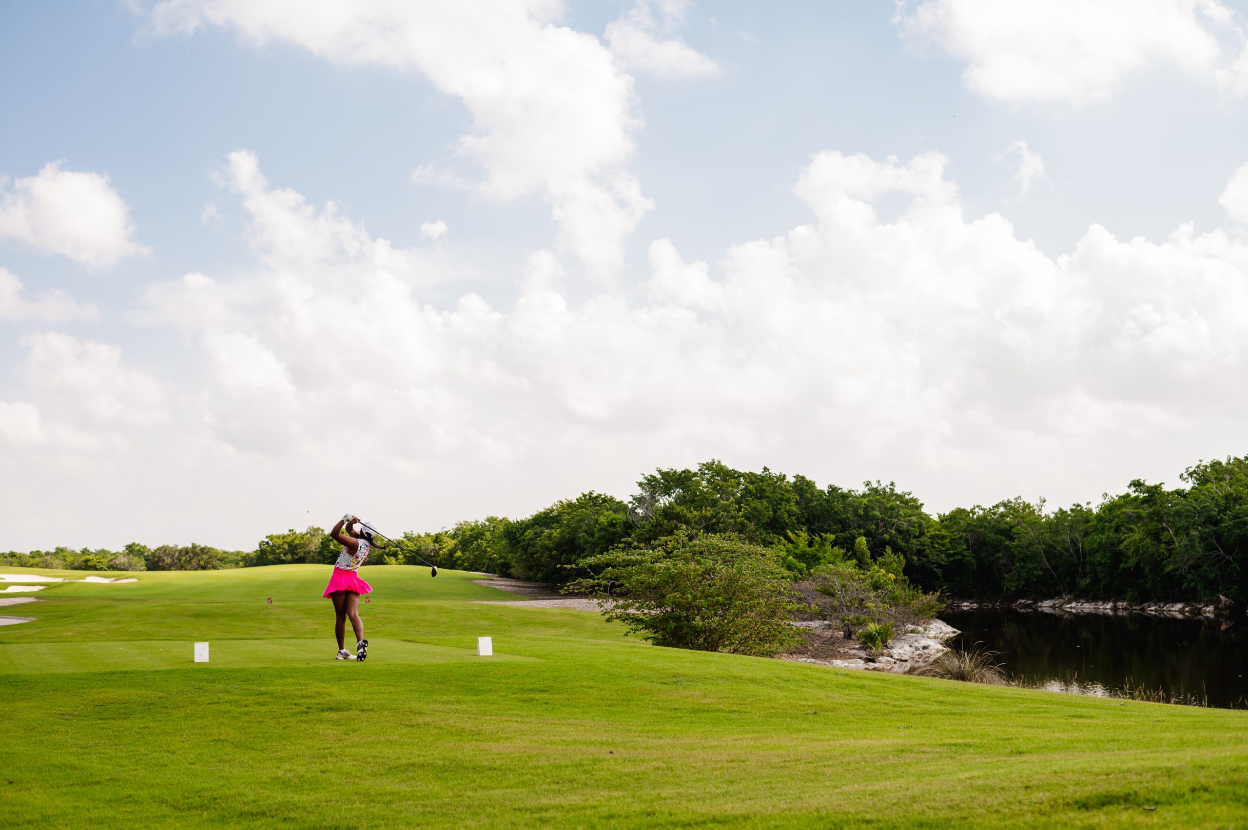 A lady playing golf gracefully on vibrant, green, well-maintained grassy ground.