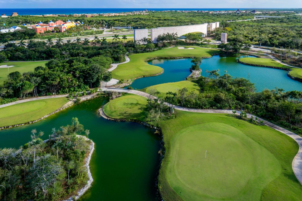 Aerial photo of lake encircled by lush, vibrant green landscape and trees.