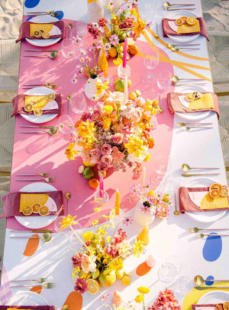 Una vista aérea de la mesa de comedor junto al mar, bellamente adornada con vajilla y flores.