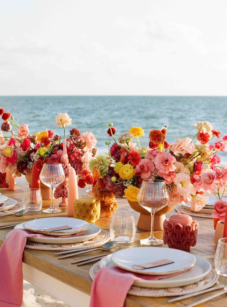 Una mesa de comedor para bodas, totalmente decorada con jarrones de flores y vajilla, ofrece una maravillosa vista del océano.