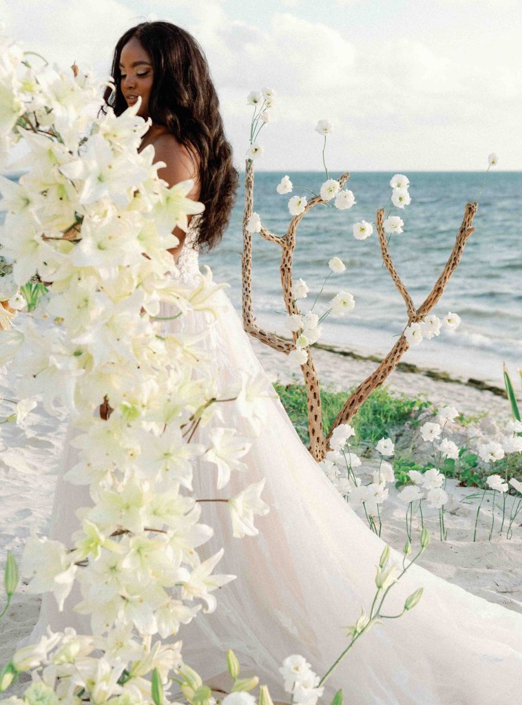 Una dama vestida de blanco se detiene con gracia ante la elegante decoración de una boda en la playa.