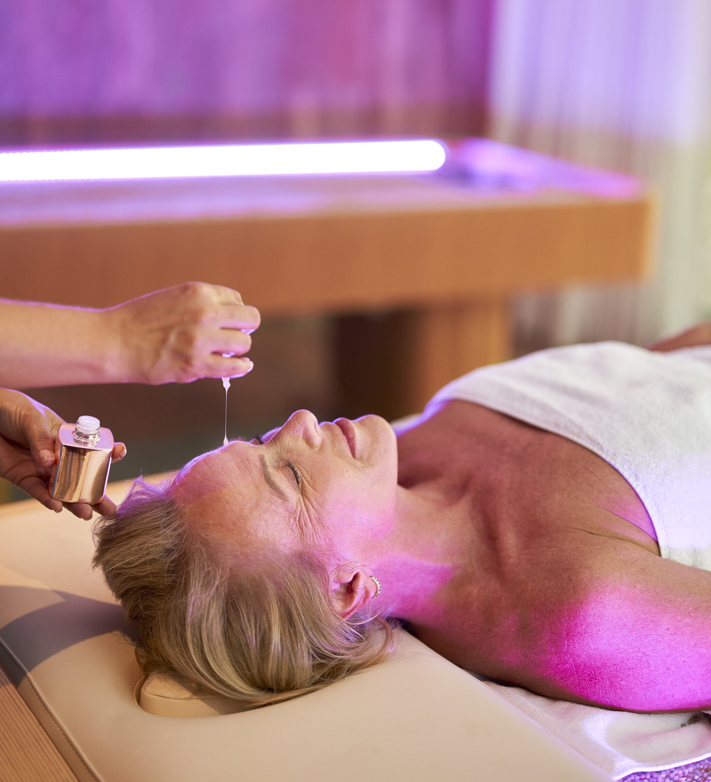A lady lies relaxed on the spa bed while another applies oil to her head.