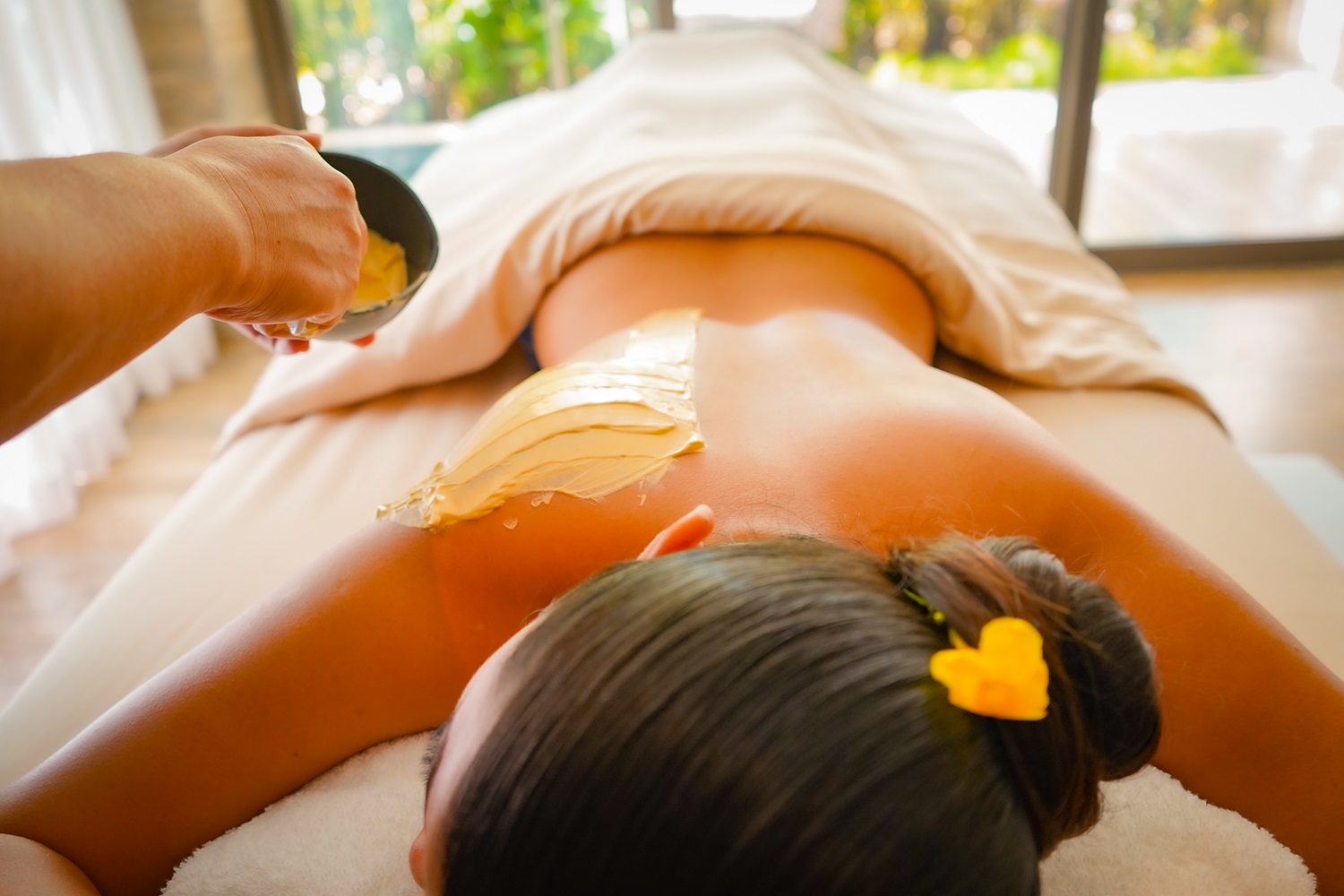 A lady lies relaxed on the spa bed while another applies soothing cream.