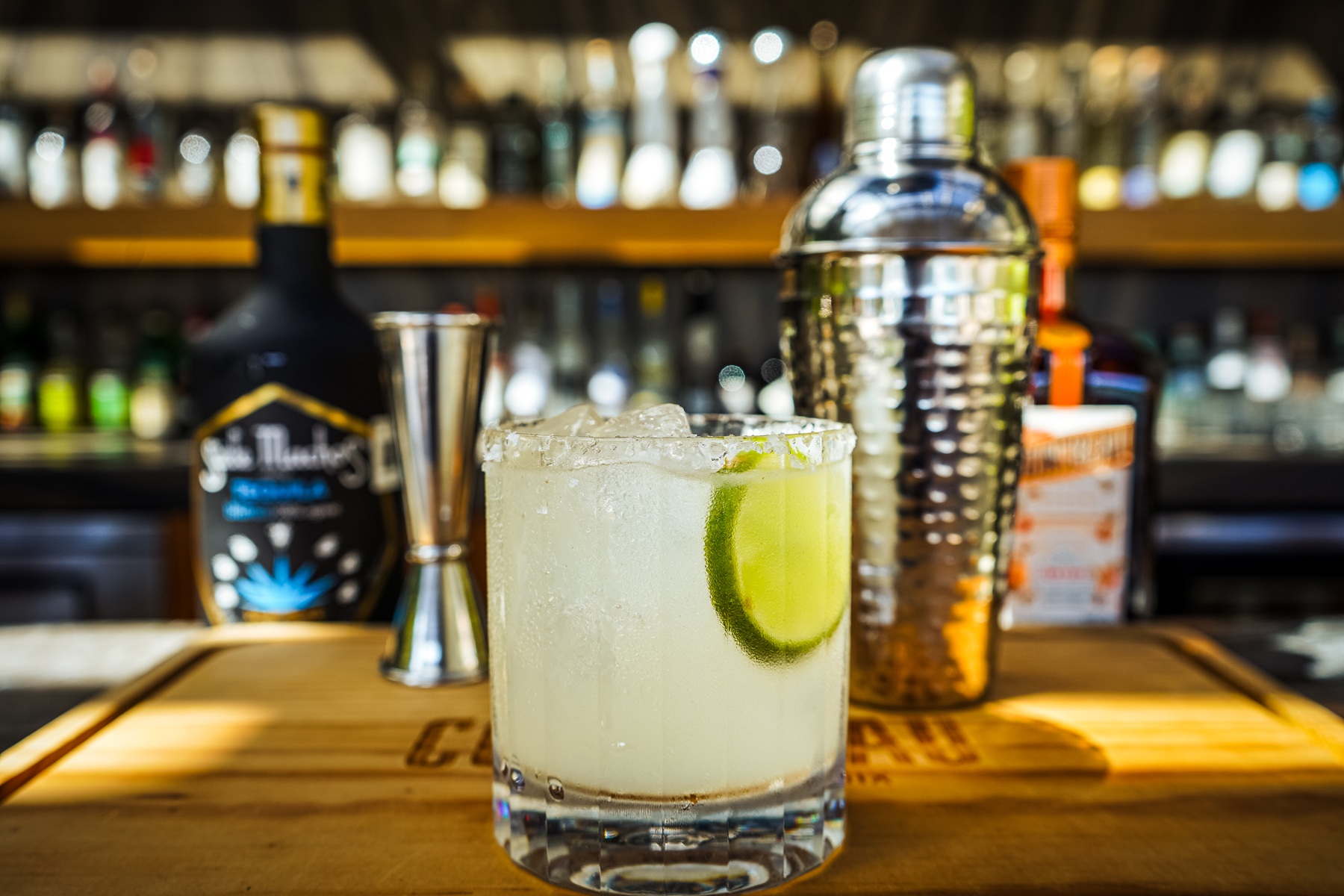 A margarita glass sits on the bar counter beside whiskey and ice bucket.