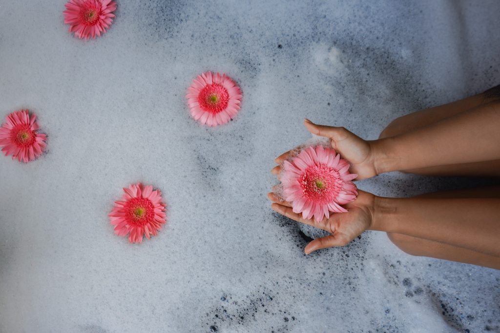 Gerbera daisies float in the jacuzzi while a person gently holds one flower.