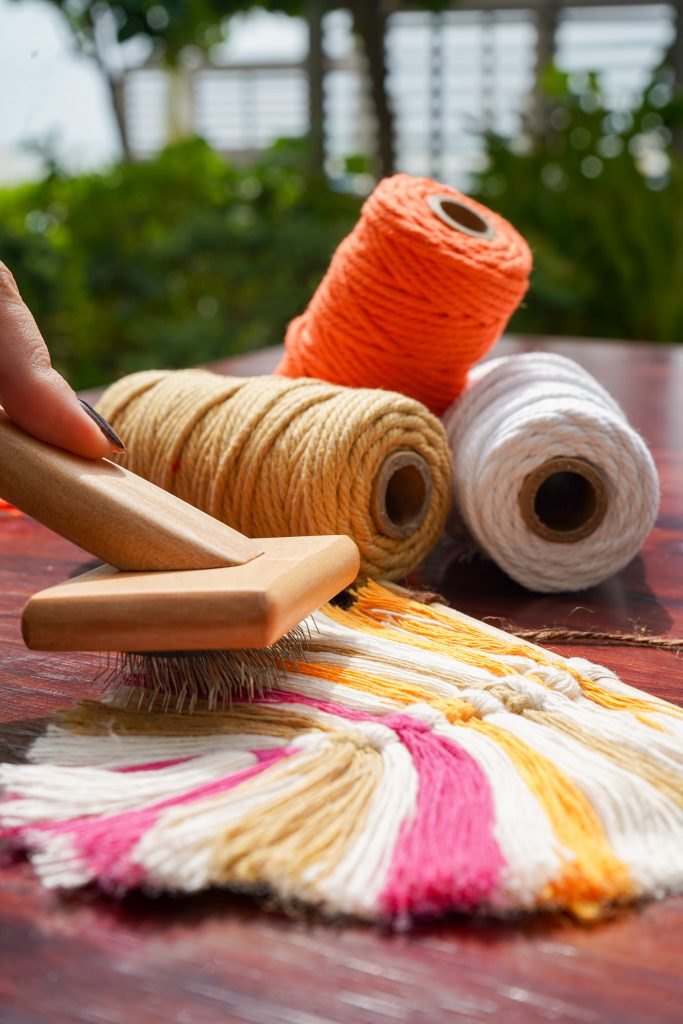 A hand carefully straightens the woolen thread using a brush for crafting purposes.
