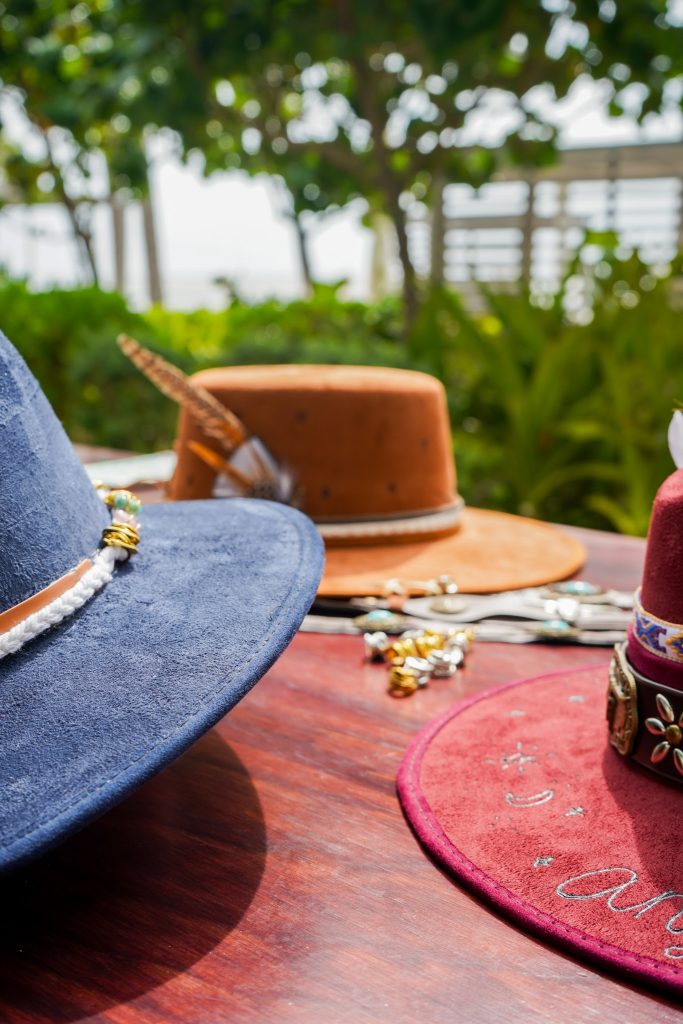 Different types of crafted hats are neatly placed on the table beneath sunlight.