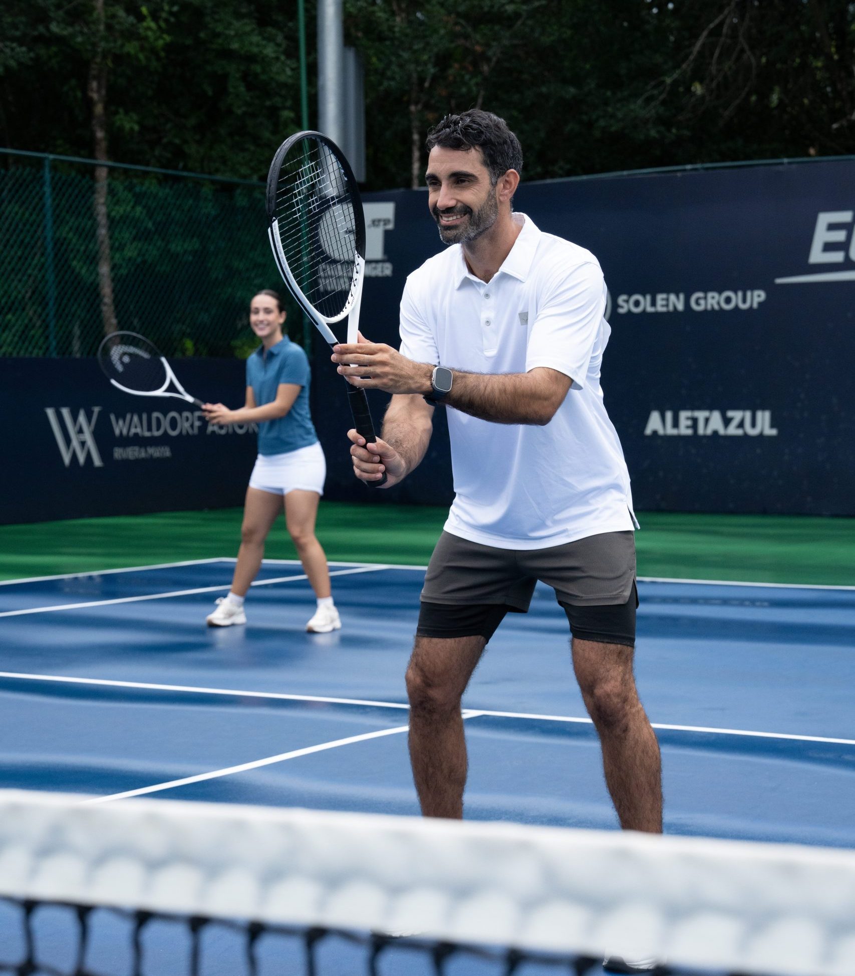 Man holding a tennis racket near the net while another player stands behind him.
